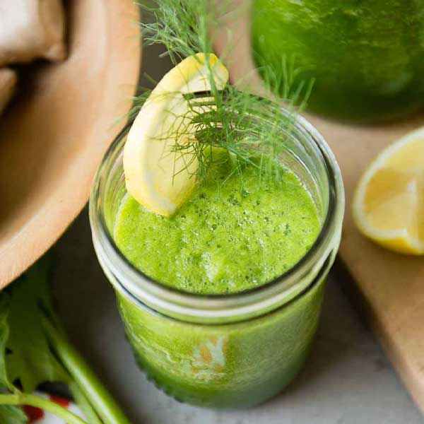 green smoothie with lemon wedge on kitchen counter.