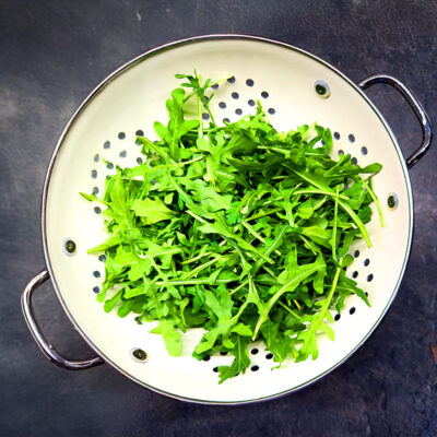 Arugula leafy greens in a white colander.