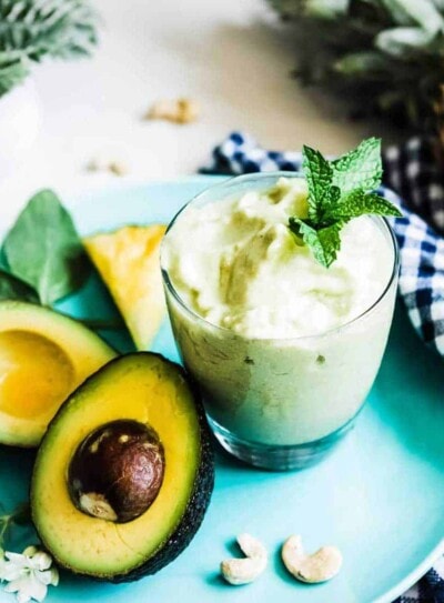 Creamy avocado smoothie recipe in a glass on a plate with fresh ingredients.