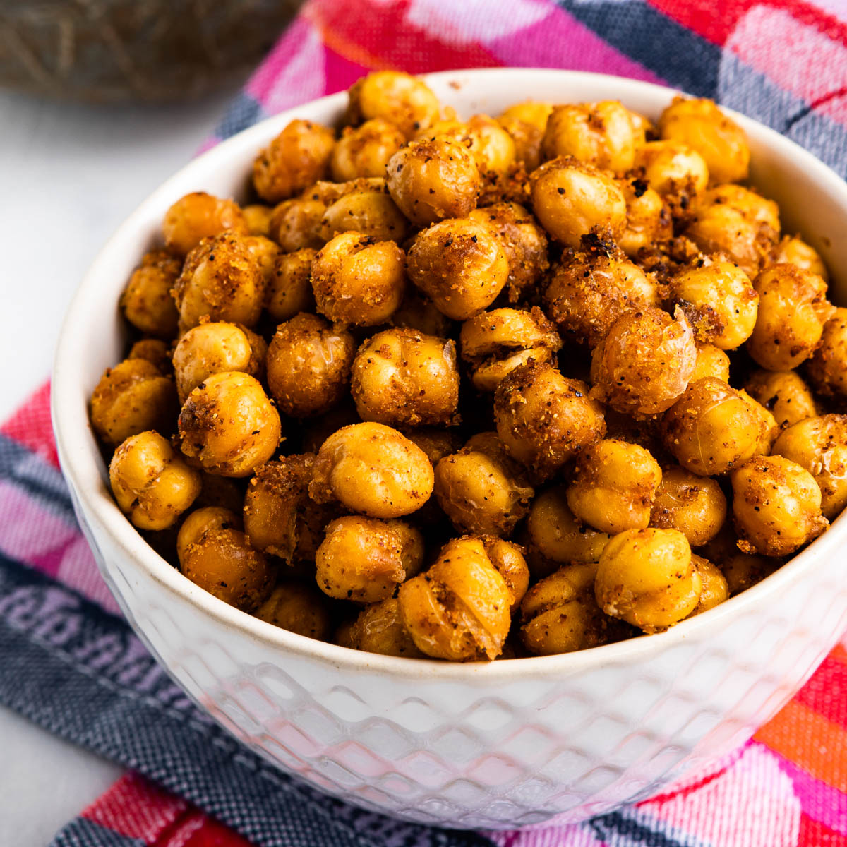 white bowl full of garlic baked chickpeas on top of a colorful tea towel.