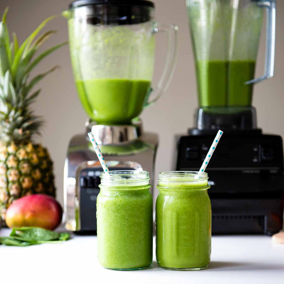 Glass of green smoothie in front of Oster blender and Vitamix blender.