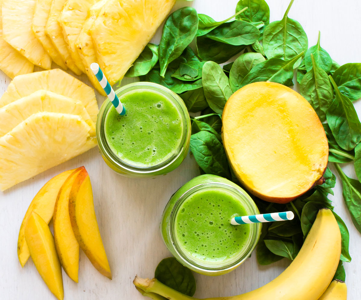 Two green smoothies in glass jars with paper straws.