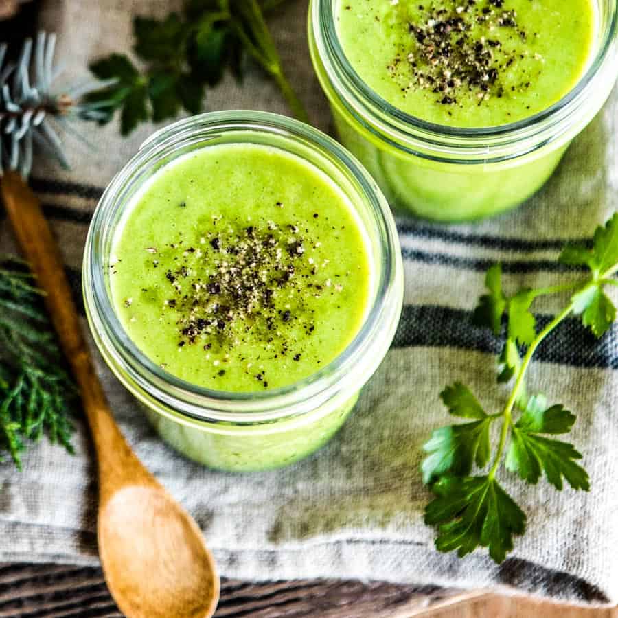 blended vegetable soup recipe in 2 glass mugs with wooden spoons.