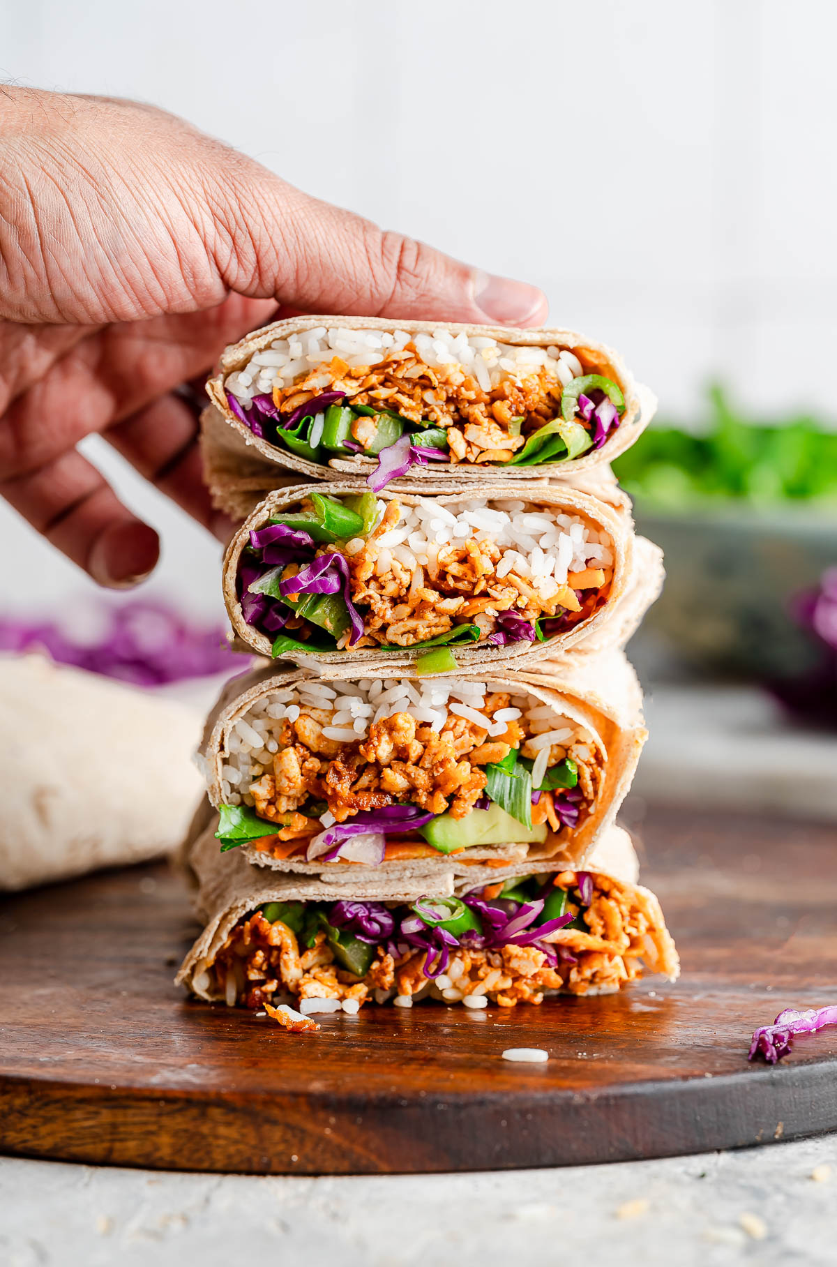 Hand carefully stacking four halves of vibrant shredded tofu wraps.
