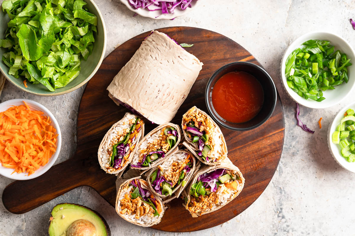Wooden cutting board with several halves of shredded tofu wraps.