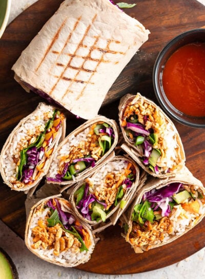 A wooden board showcases several vibrant buffalo shredded tofu wraps.
