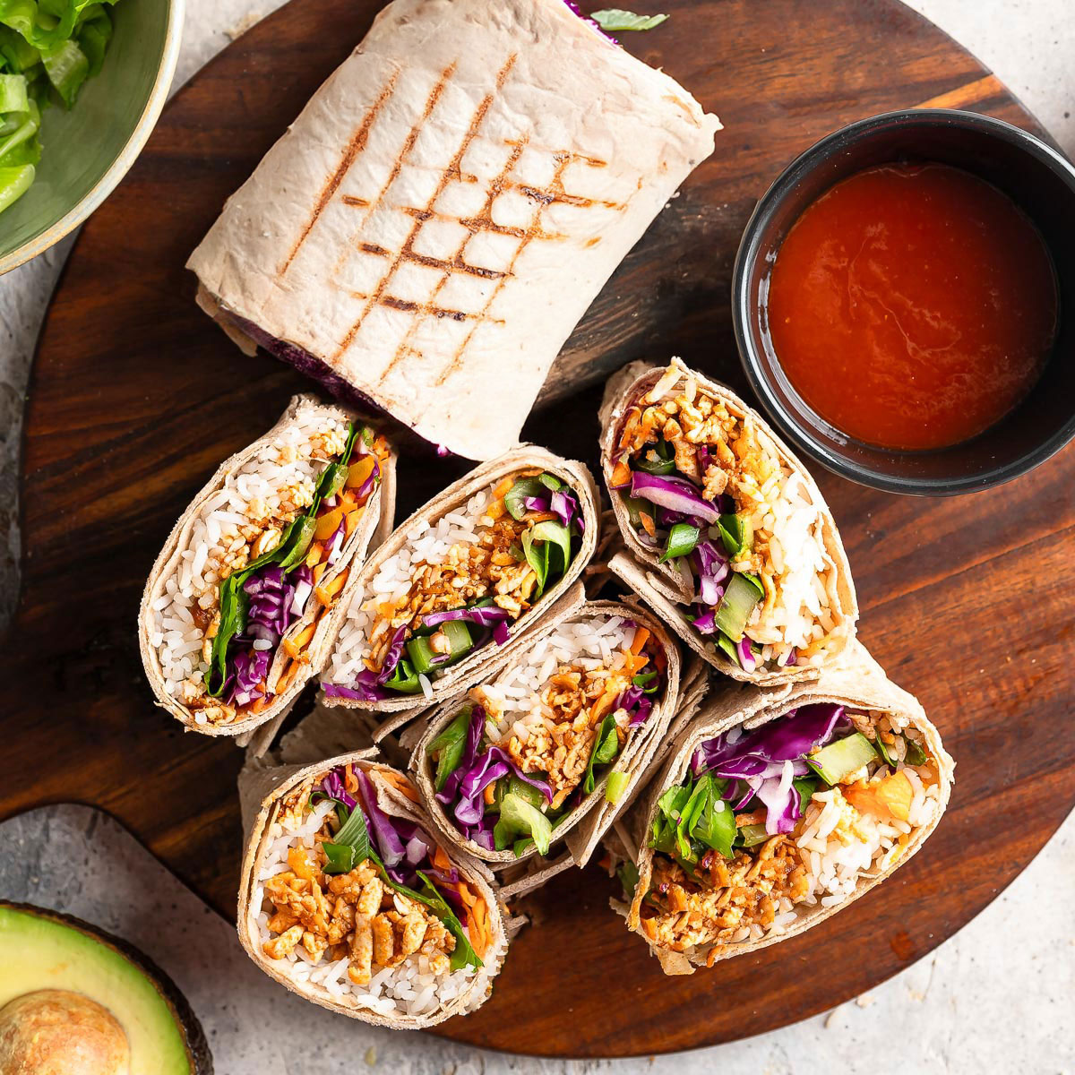 A wooden board showcases several vibrant buffalo shredded tofu wraps.