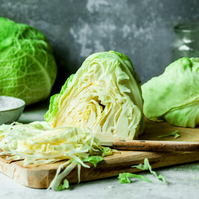 Cabbage head on wood cutting board with a knife.