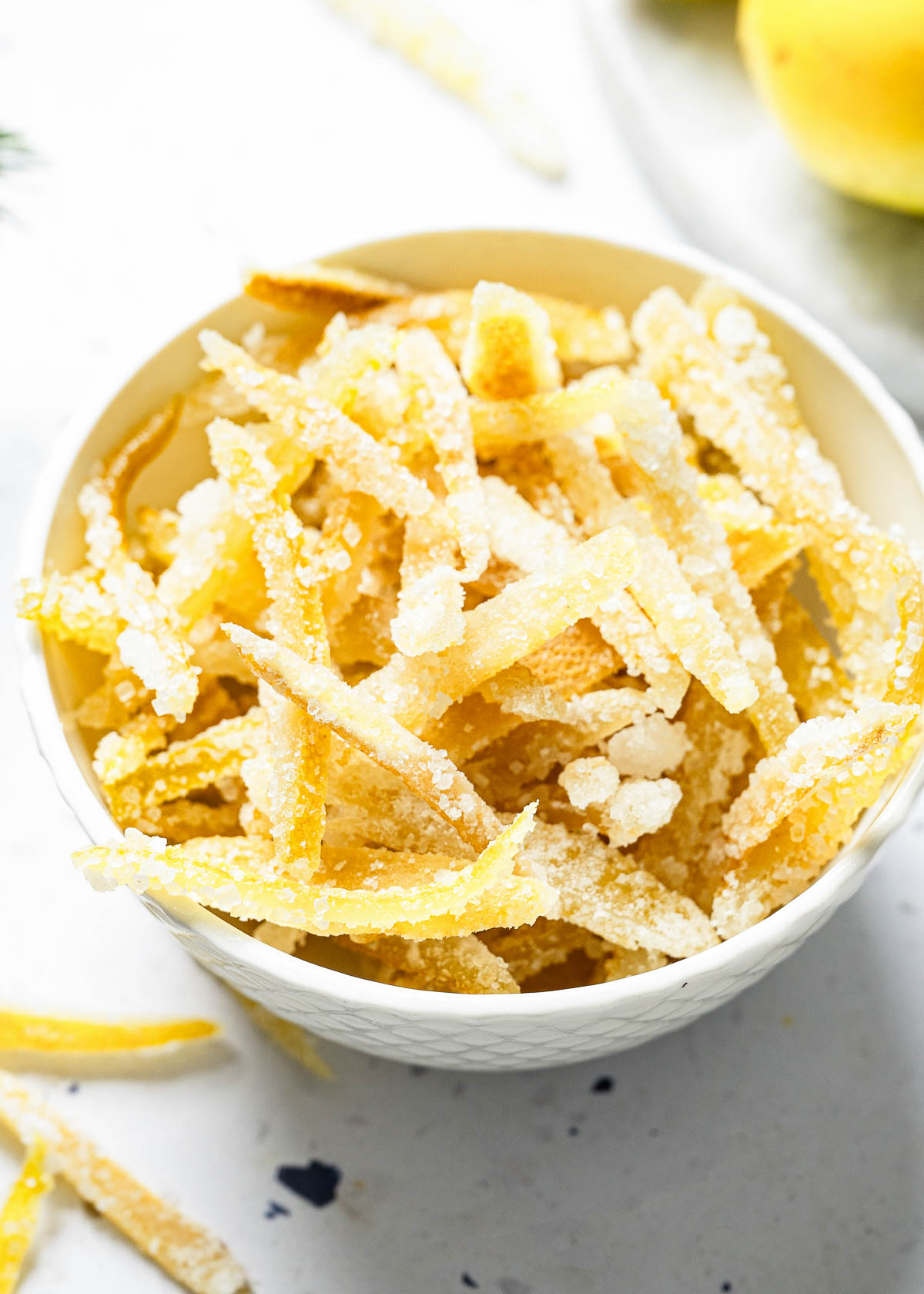 A white bowl filled with bright candied lemon peels.