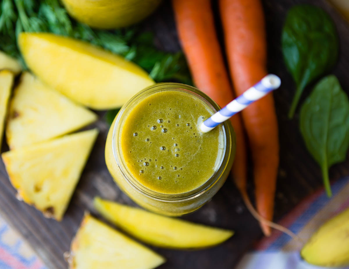 Glass of blended carrot greens smoothie with carrot tops on counter.