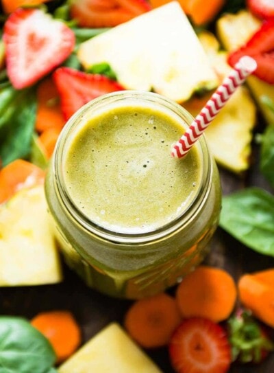 strawberry carrot smoothie in a mason jar with a paper straw surrounded by fresh ingredients.