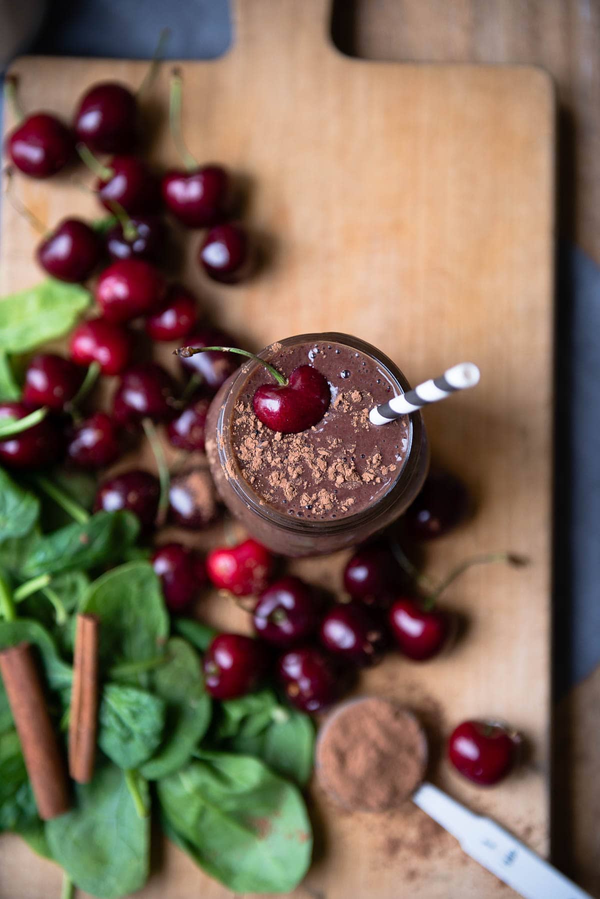 Chocolate smoothie with paper straw and topped with cacao and a fresh cherry.