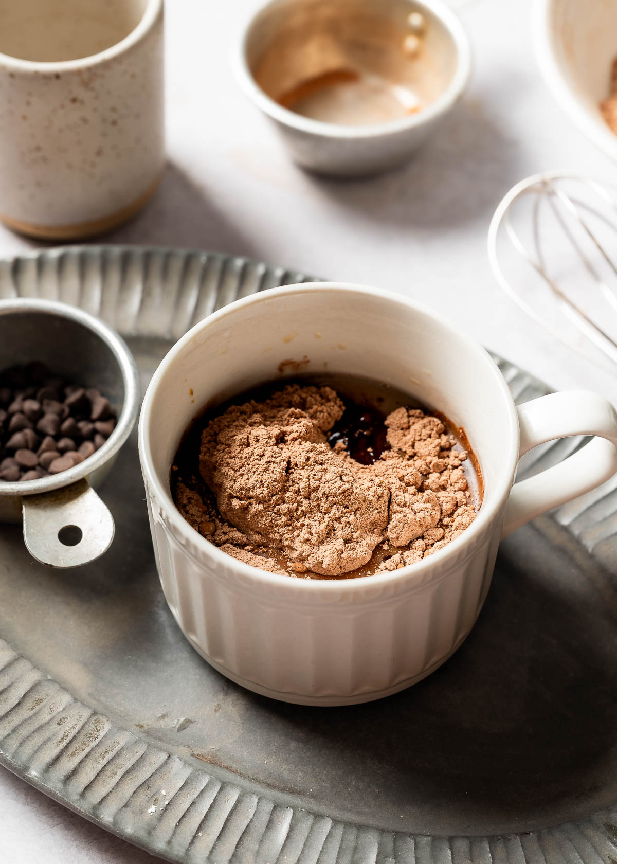 Mug with cacao powder, chocolate chips and flour with a whisk.