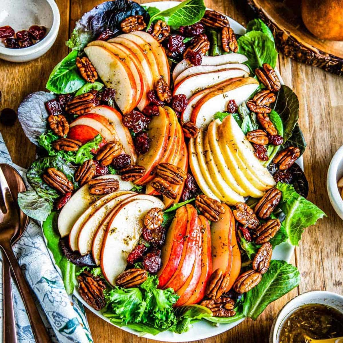 platter of fall salad featuring a bed of mixed greens topped with sliced apples, pears, candied pecans, dried cherries and a vinaigrette.
