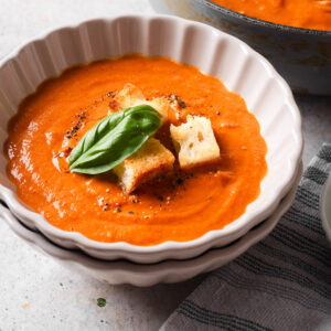 Bowl a fire-roasted tomato soup with croutons and fresh basil leaf on top.