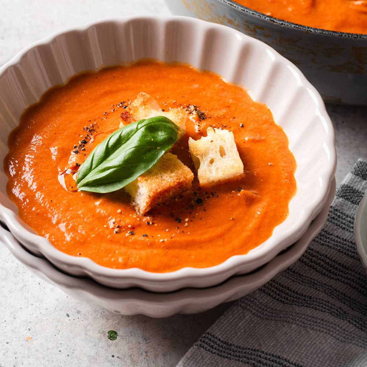 Bowl a fire-roasted tomato soup with croutons and fresh basil leaf on top.