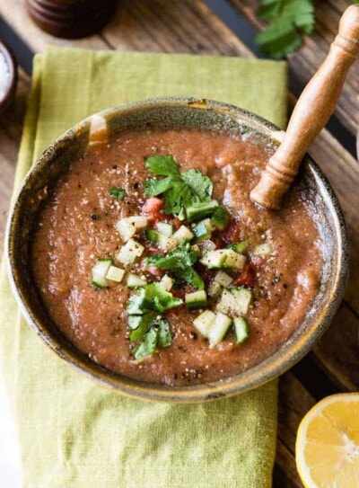 Blended easy gazpacho soup recipe in ceramic bowl on green cloth napkin.