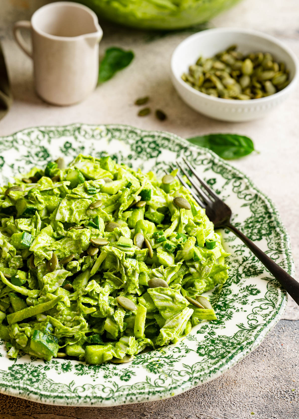 A plate of green goddess salad with a bowl of pumpkin seeds.