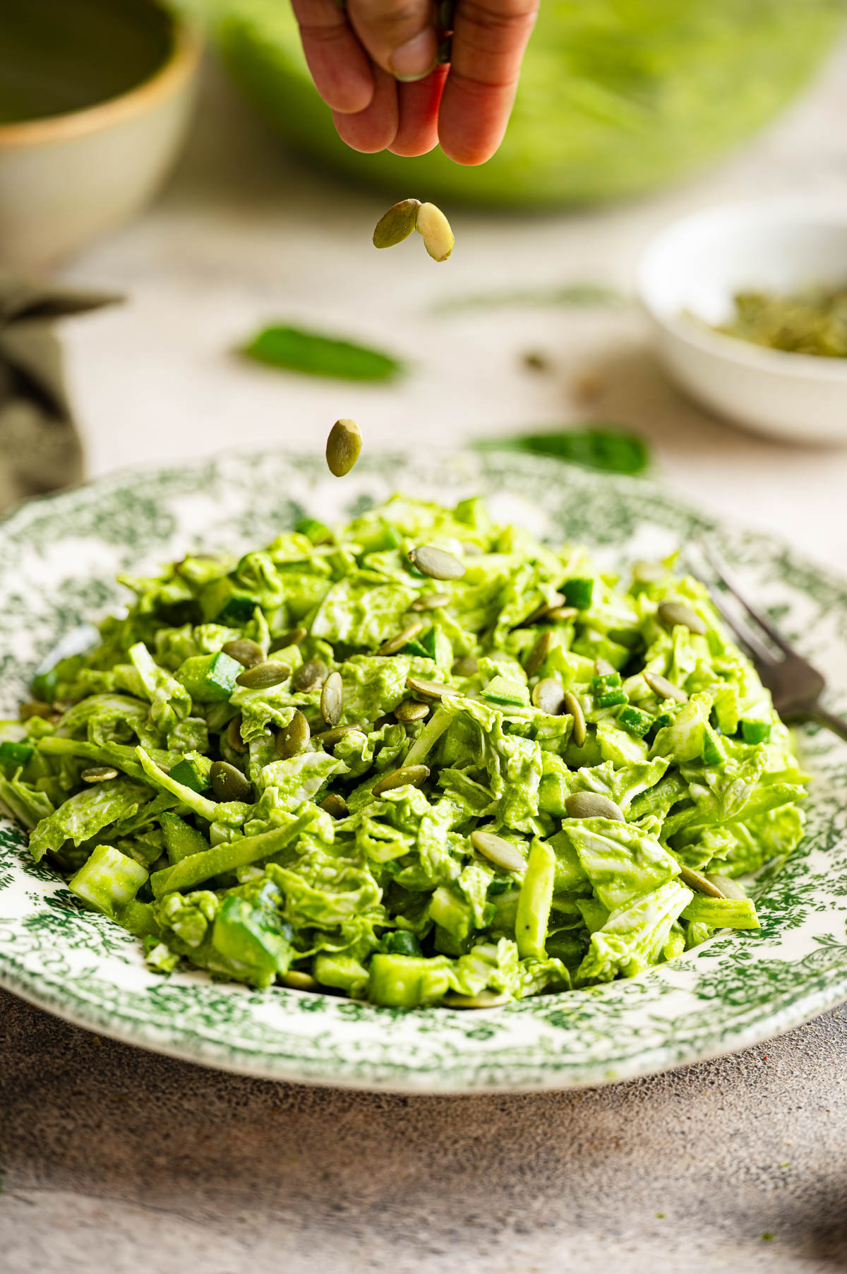A person sprinkling pumpkin seeds on the green goddess salad.
