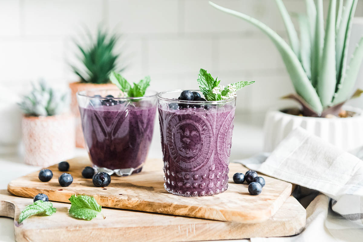 Two glasses full of healthy blueberry smoothies topped with fresh fruit and mint.