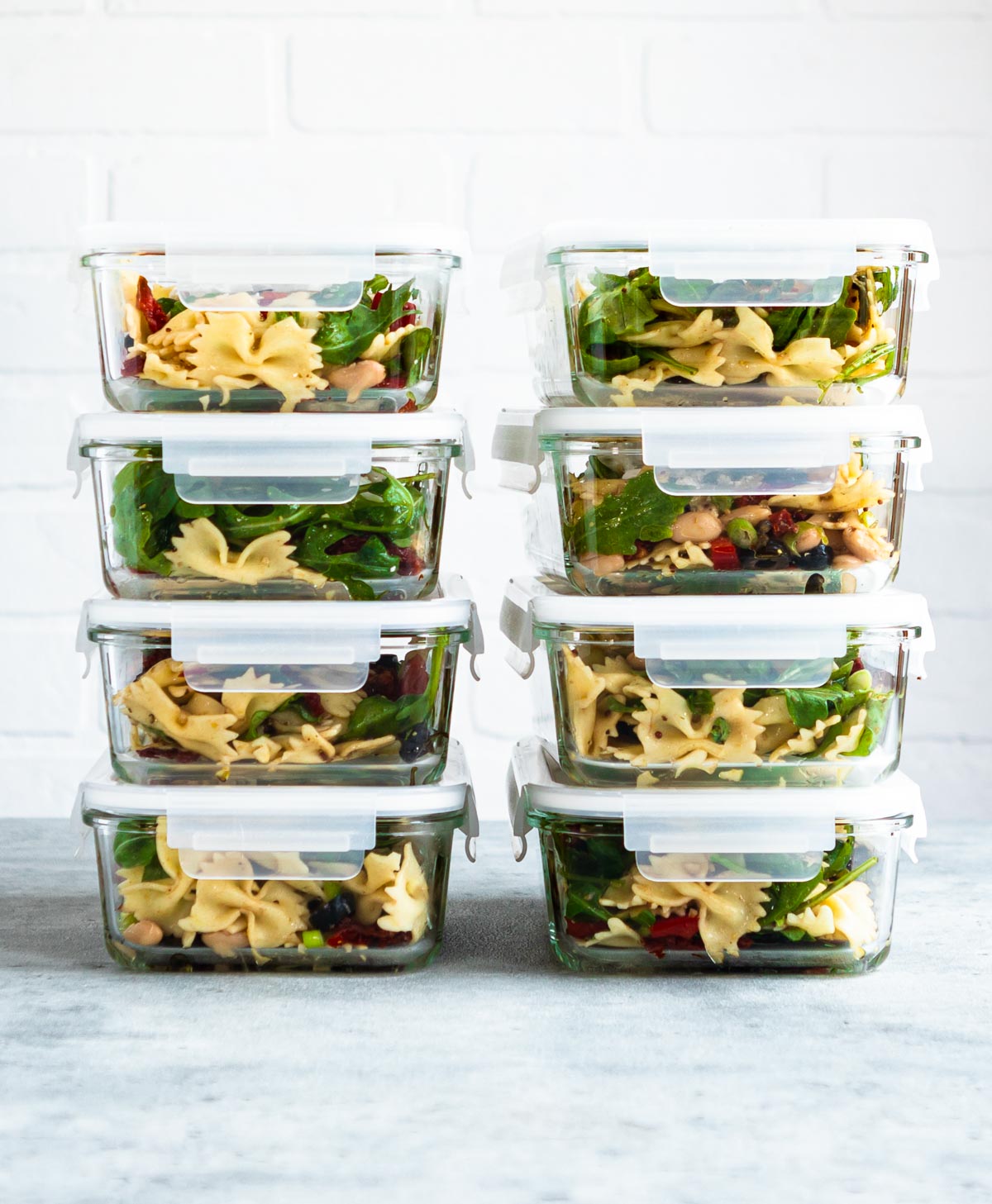 Healthy pasta salad recipe in meal prep containers stacked on counter.