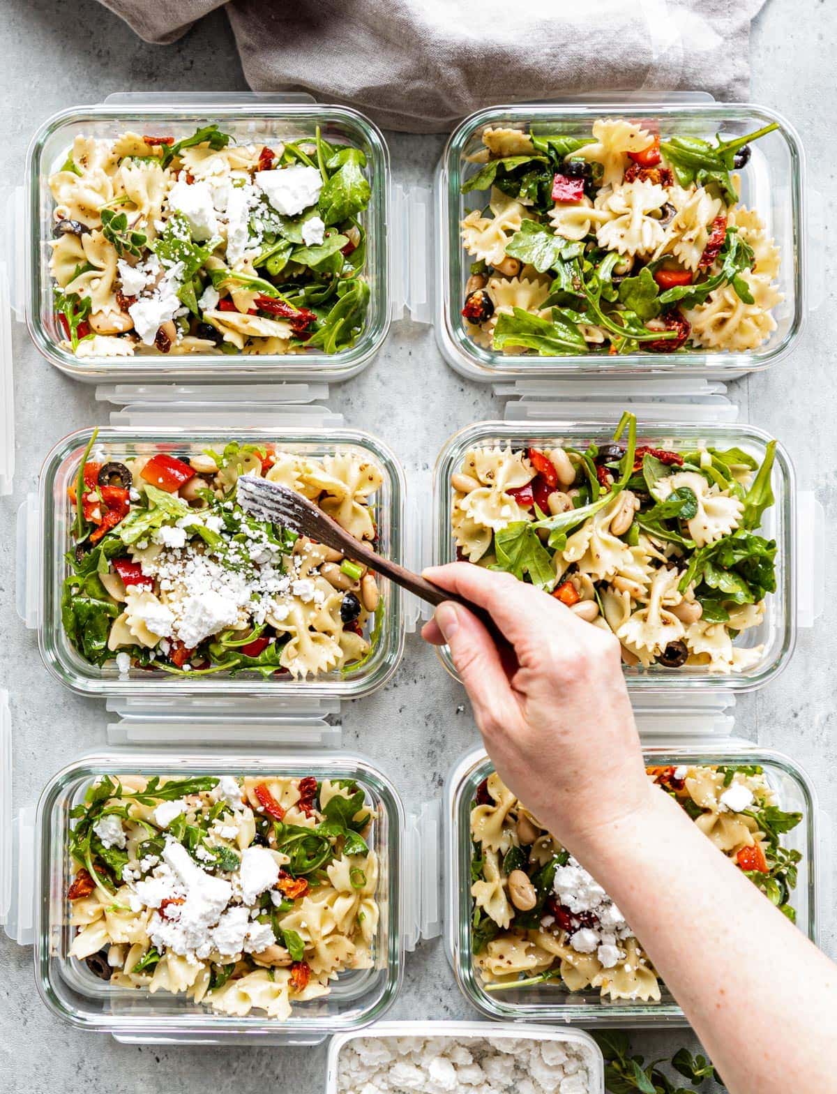 Glass containers lined up with healthy pasta salad.