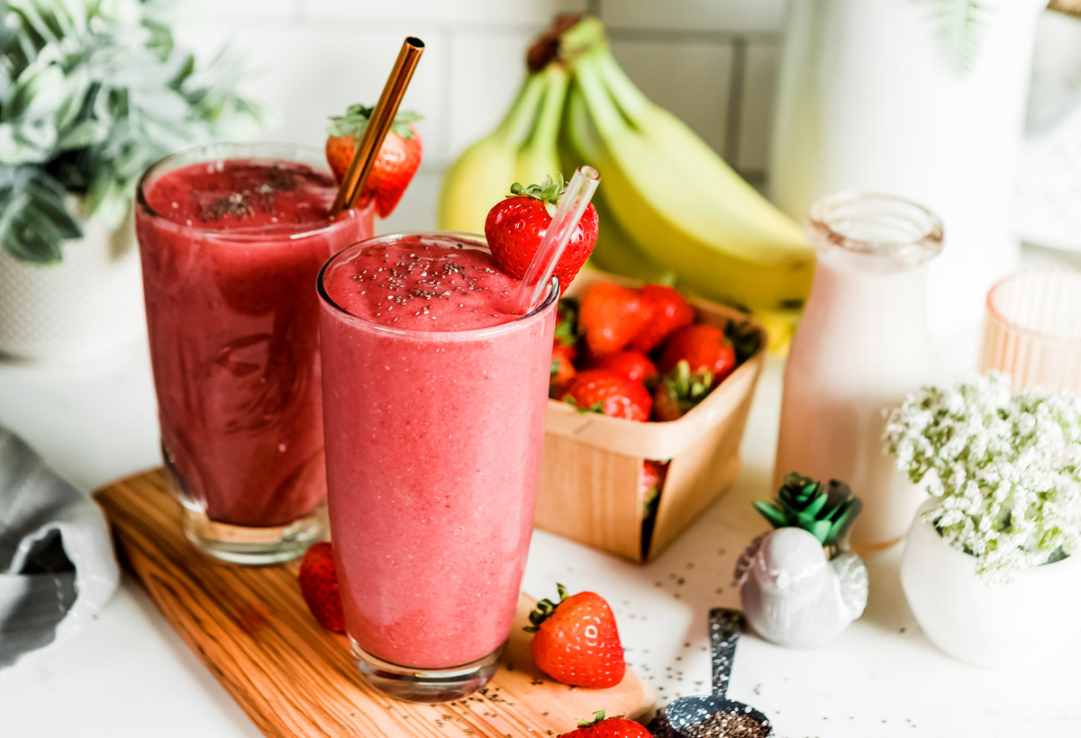 Two red glasses of smoothie on table with fresh strawberries in a basket.