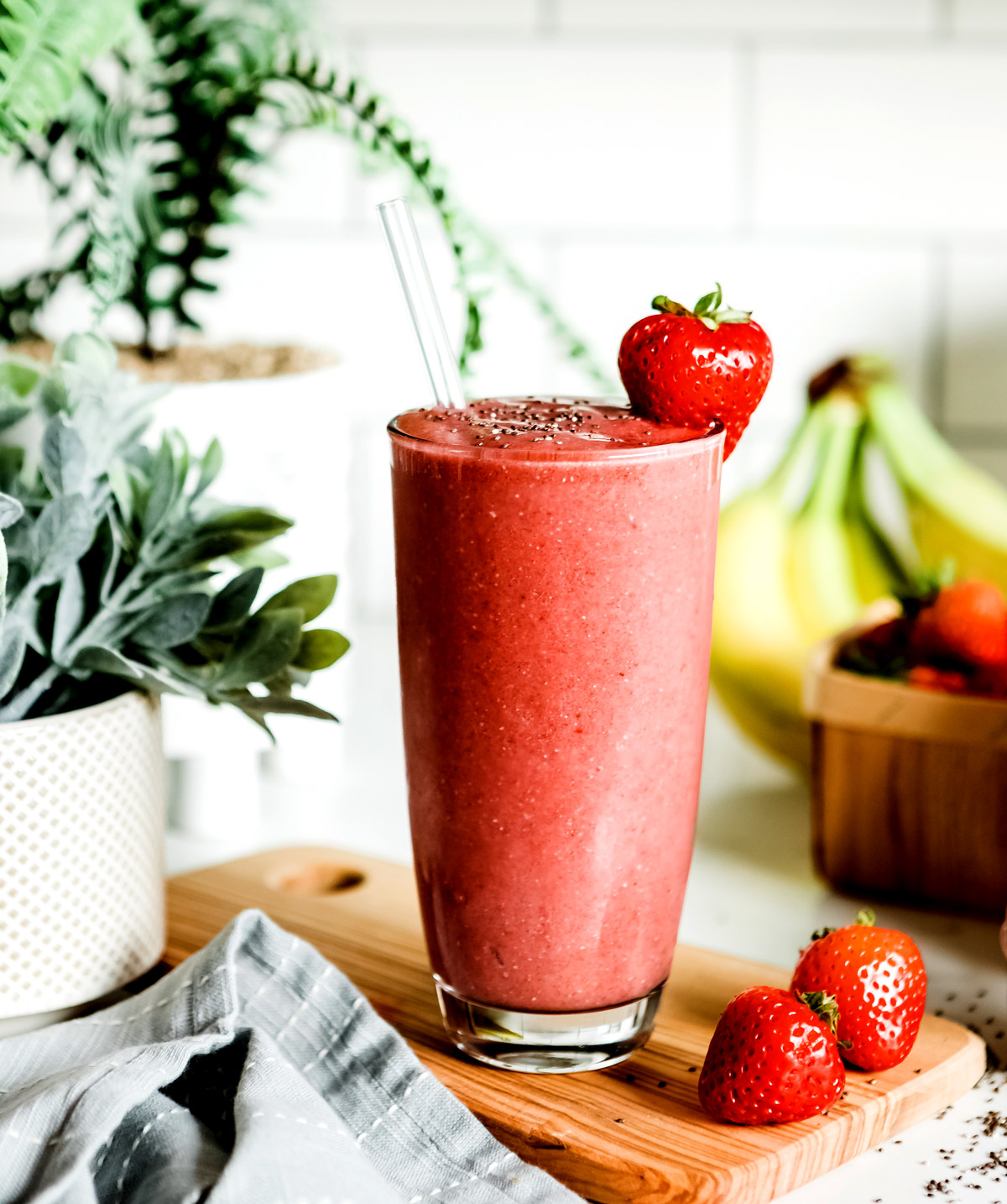 Close up of a strawberry banana smoothie with a glass straw and strawberry garnish.