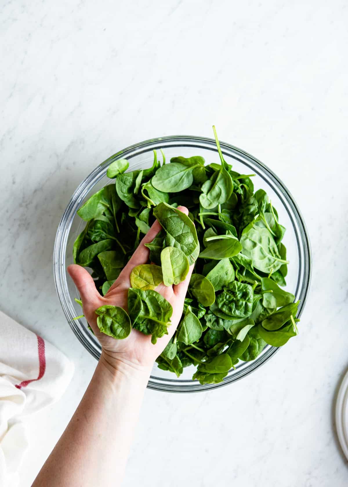 Handful of spinach over a glass bowl of fresh spinach.