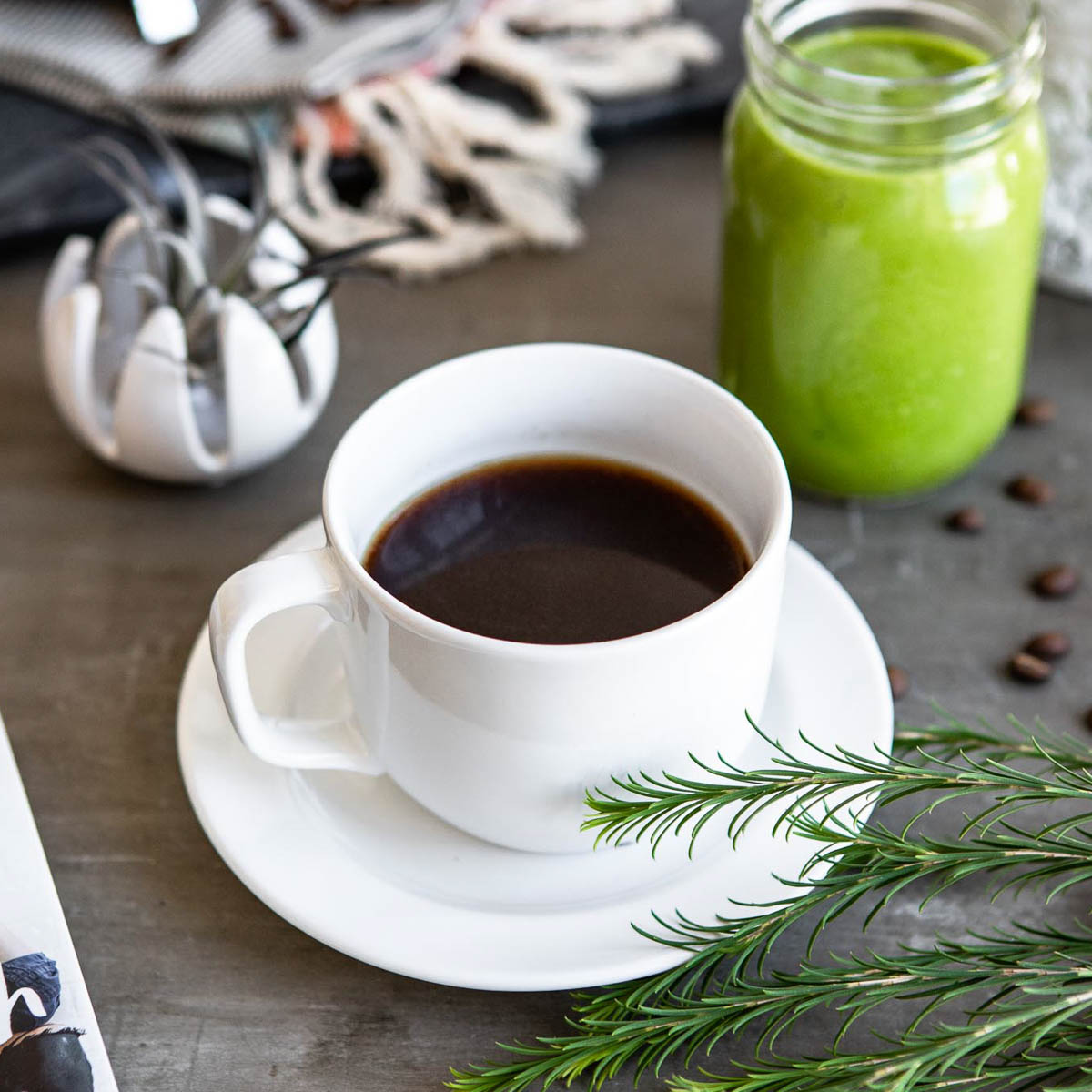 healthy coffee in a white cup on a white plate next to a jar of green smoothie.