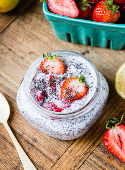 strawberry lemon chia pudding in a glass jar next to fresh lemons and sliced strawberries.