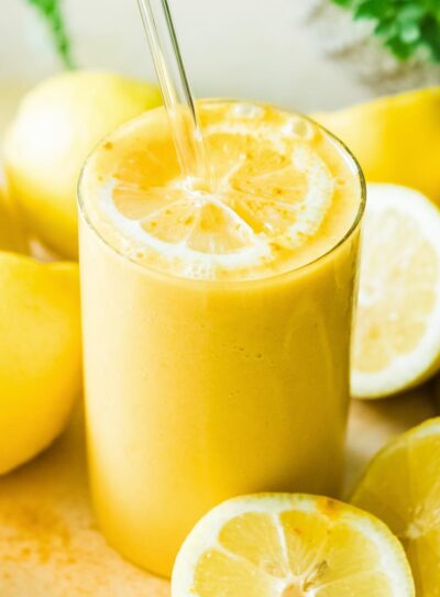 Lemon smoothie in a glass with straw surrounded by lemons.