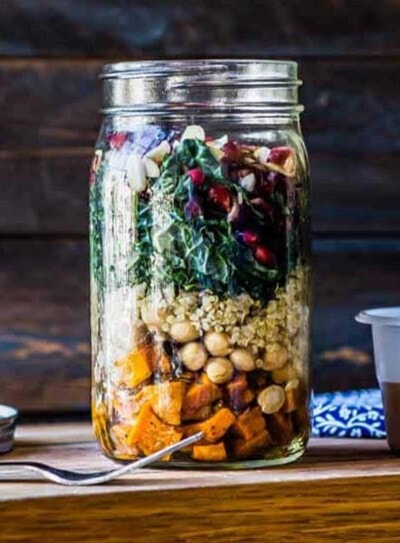 a fully layered mason jar salad with a homemade dressing next to it, ready to go