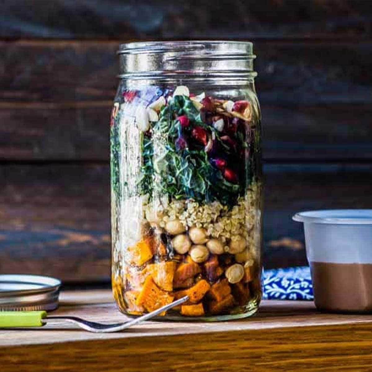 a fully layered mason jar salad with a homemade dressing next to it, ready to go
