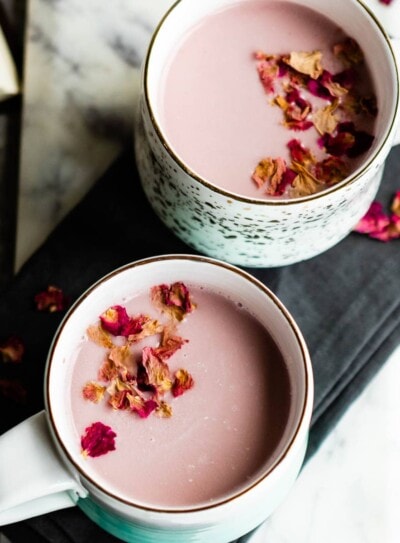 Two white mugs filled with pink moon milk, garnished with culinary rose petals.