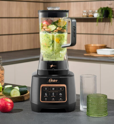 Oster blender in kitchen with glass of smoothie on counter.