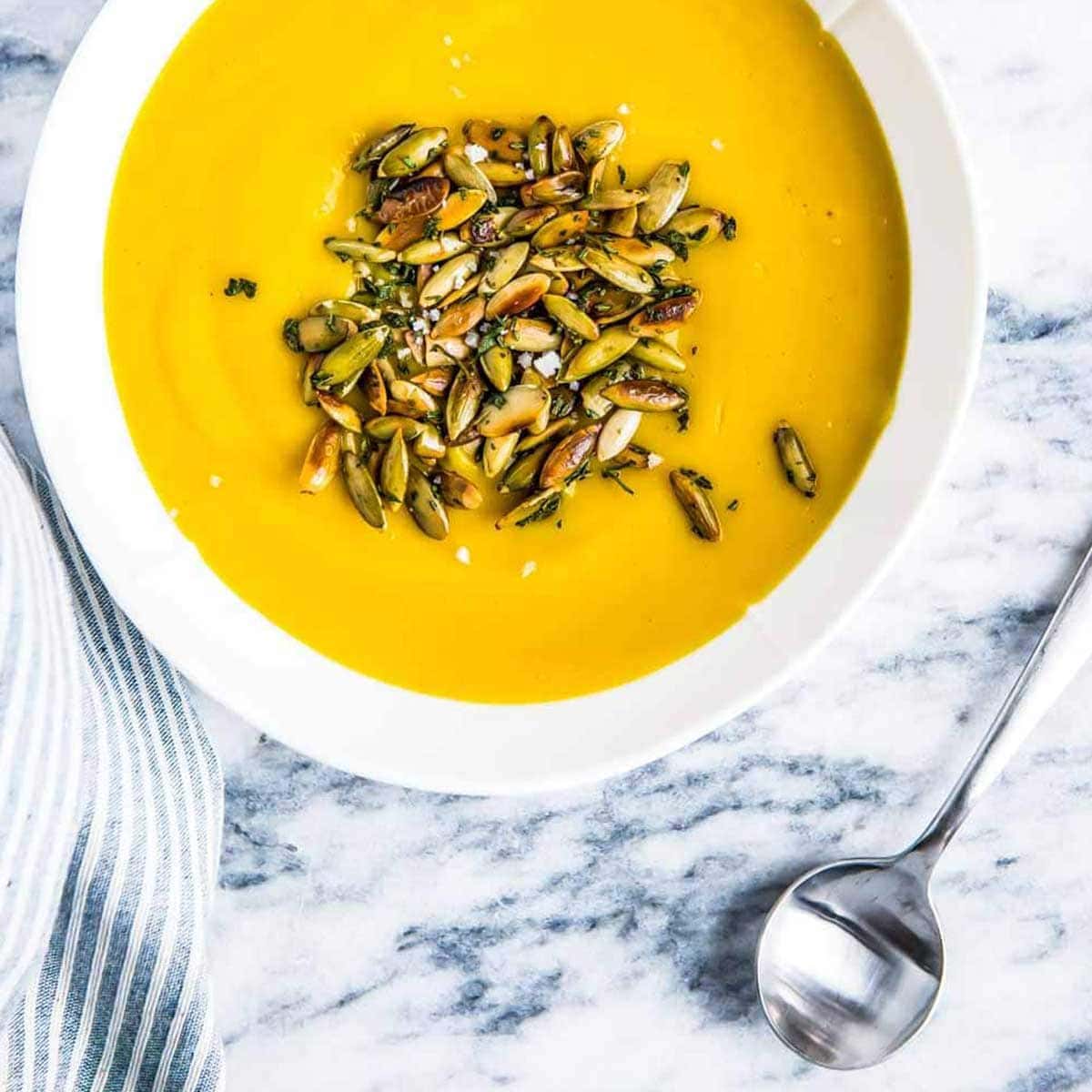 white bowl full of vegan pumpkin soup topped with roasted pumpkin seeds, on a marble counter top.