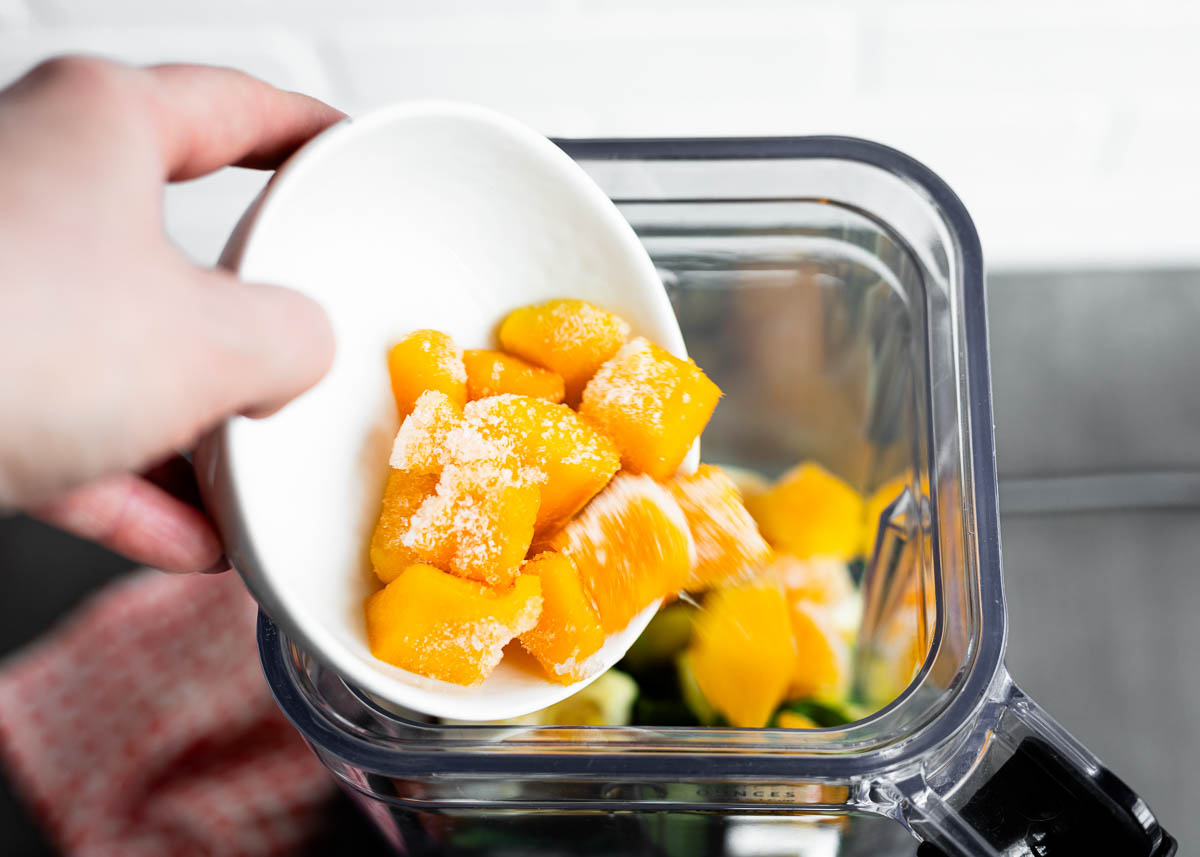 Frozen mango being poured into a blender for a spirulina smoothie.