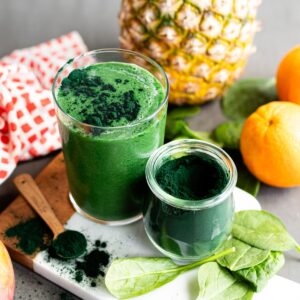 A green spirulina smoothie in a glass beside a jar of spirulina powder.
