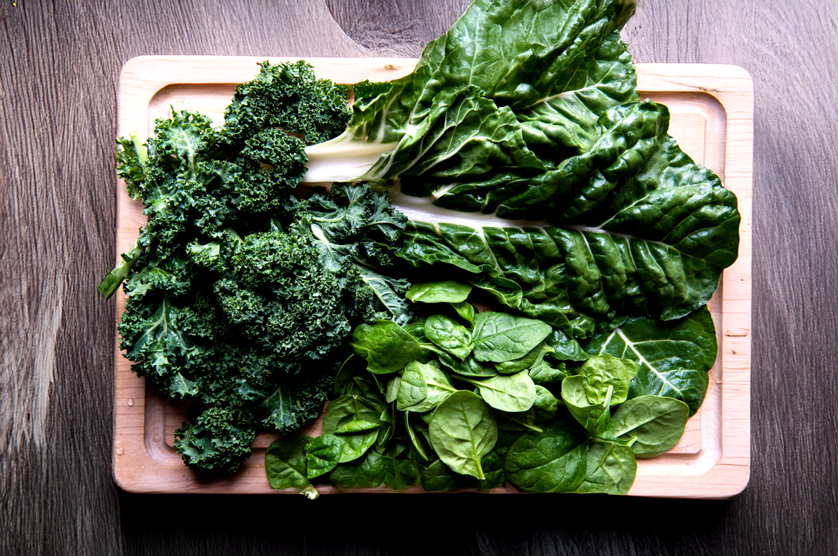 Wood cutting board with fresh leafy greens like chard, kale and spinach.