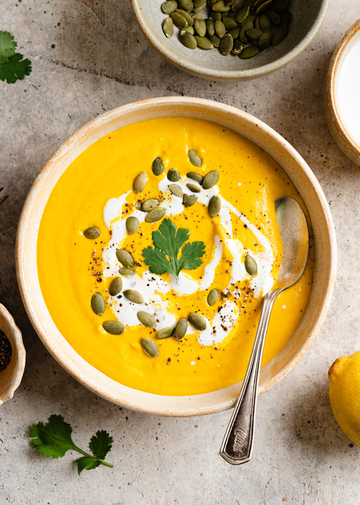 Bowl of vegan carrot ginger soup on table with drizzle of cashew cream and topped with pepitas.