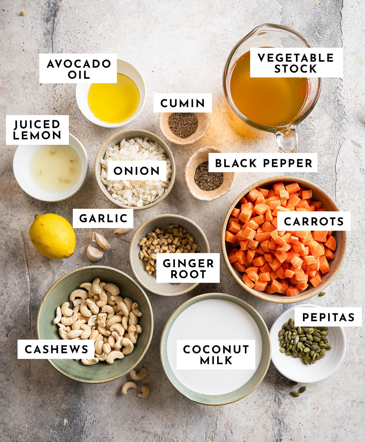 Ingredients to make carrot ginger soup on textured white surface with beautiful bowls.