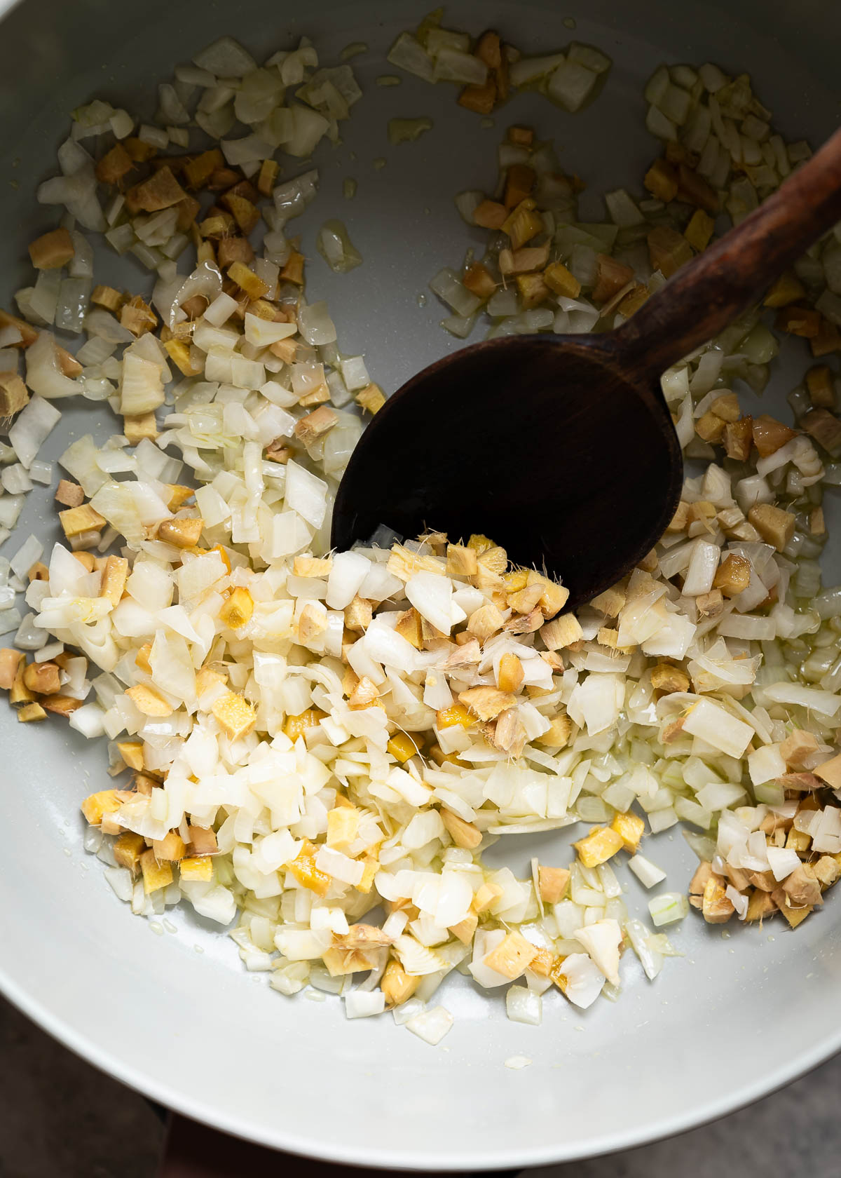Onions and ginger sautéed and skillet with a wood spoon that is stirring the ingredients.