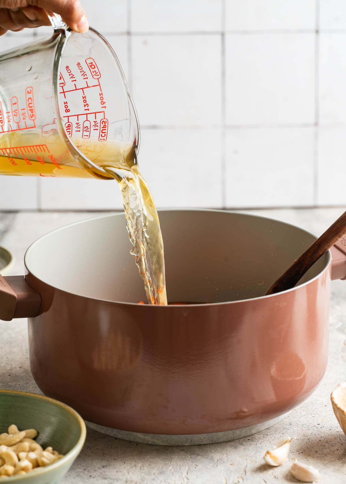 Pouring vegetable stock into a pot to make vegan carrot ginger soup recipe.