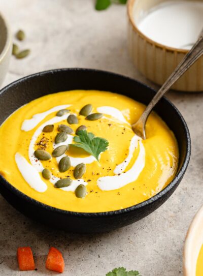 Carrot ginger Soup in a black bowl topped with swirls of cashew cream, fresh cilantro, and pepitas.