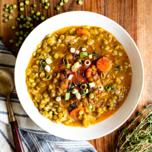 Vegetarian split pea soup in a white bowl next to a spoon on a blue striped tea towel.