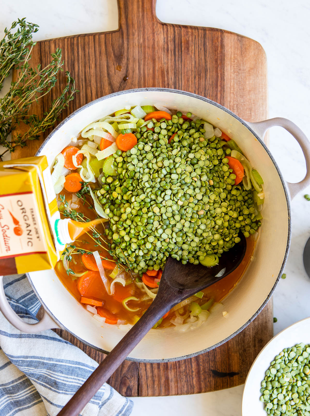 Pouring vegetable broth into a pot of vegetarian split pea soup.