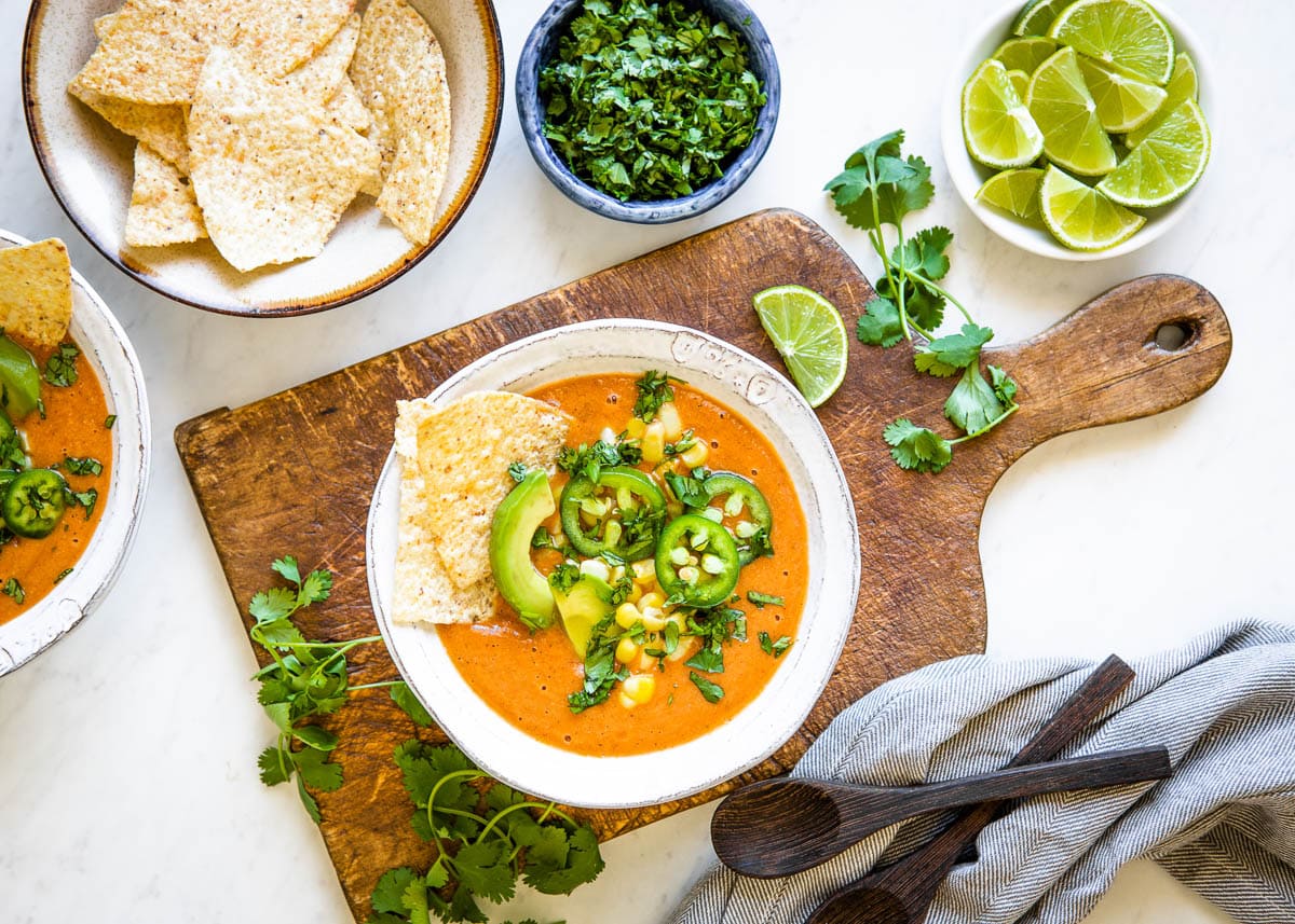 Delicious vegetarian tortilla soup in a white bowl with tortilla chips, fresh jalapeños, avocados, corn and cilantro on top.